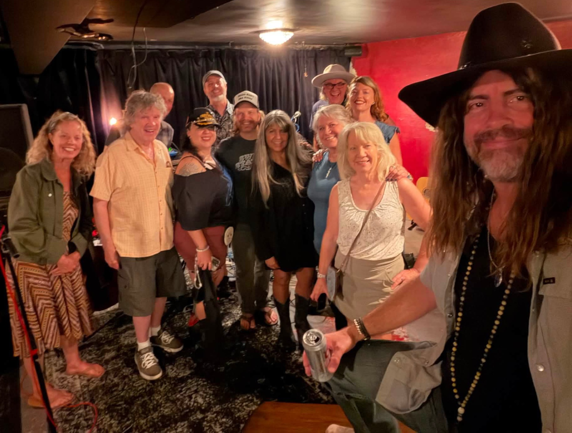 Group of people posing on stage with a man in a cowboy hat in the foreground, smiling and holding a drink.