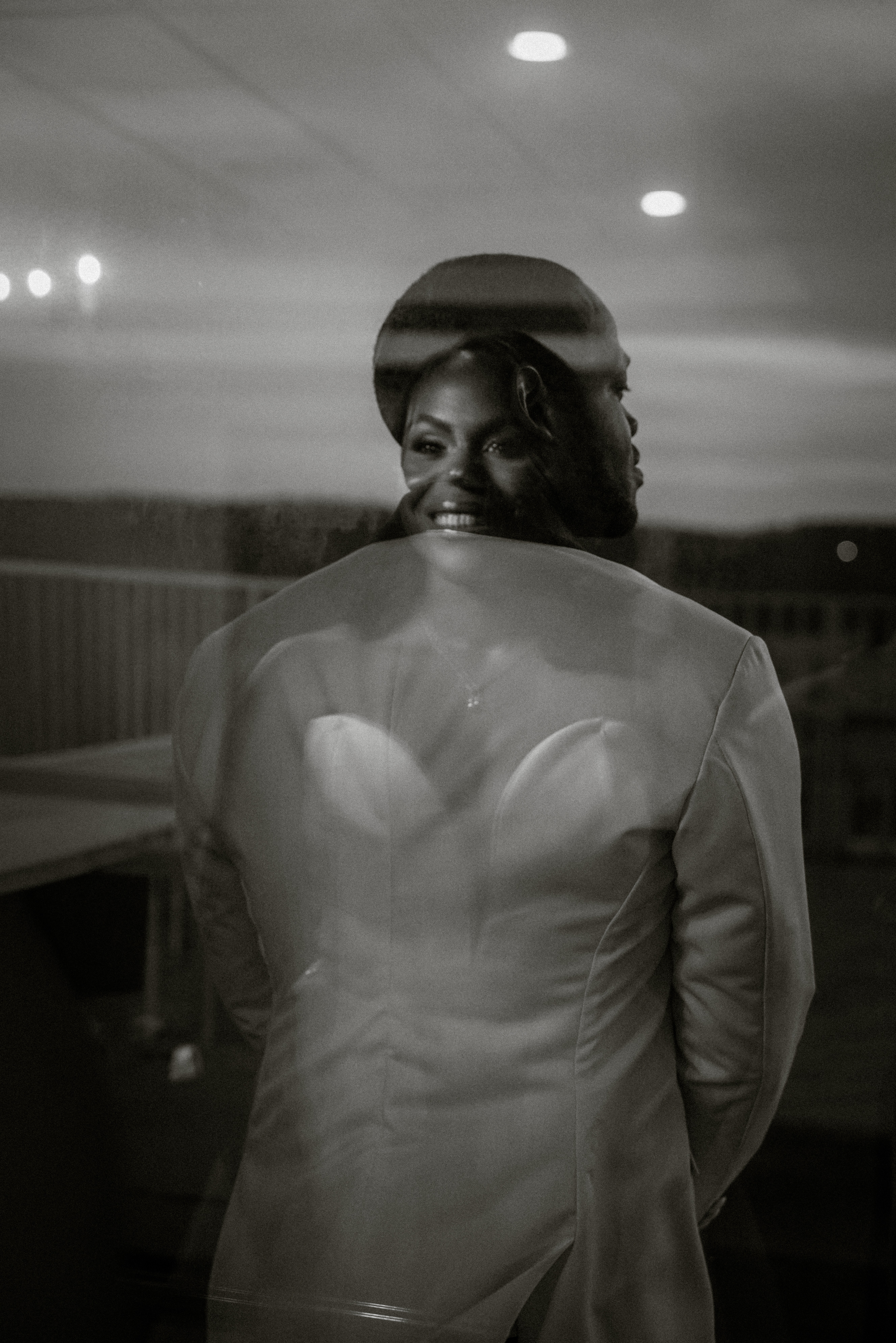 Person in a suit smiling, with a sunset or evening sky in the background, double exposure effect, black and white.