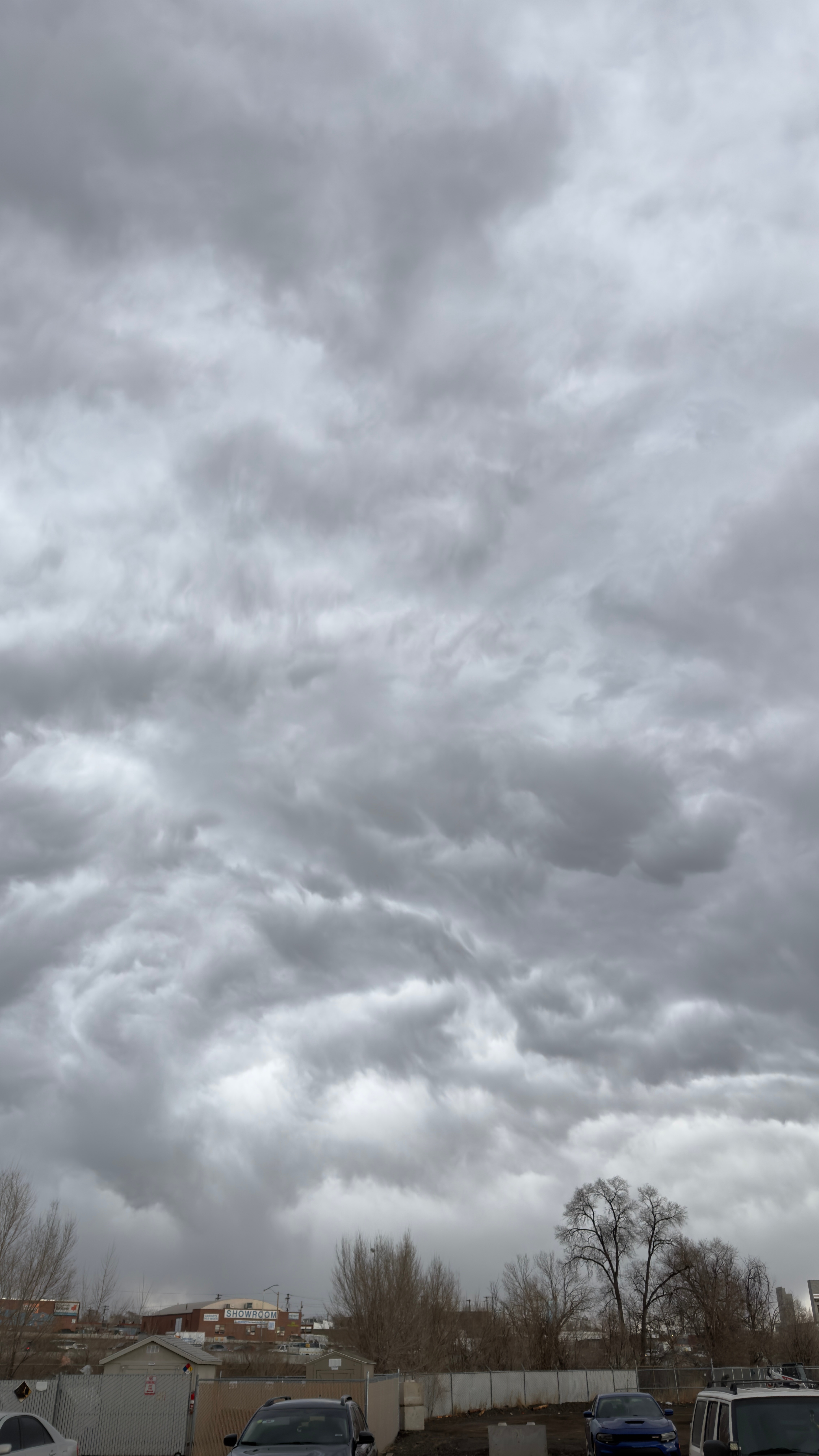 Overcast sky with dark, dense clouds and a few trees and buildings at the bottom.