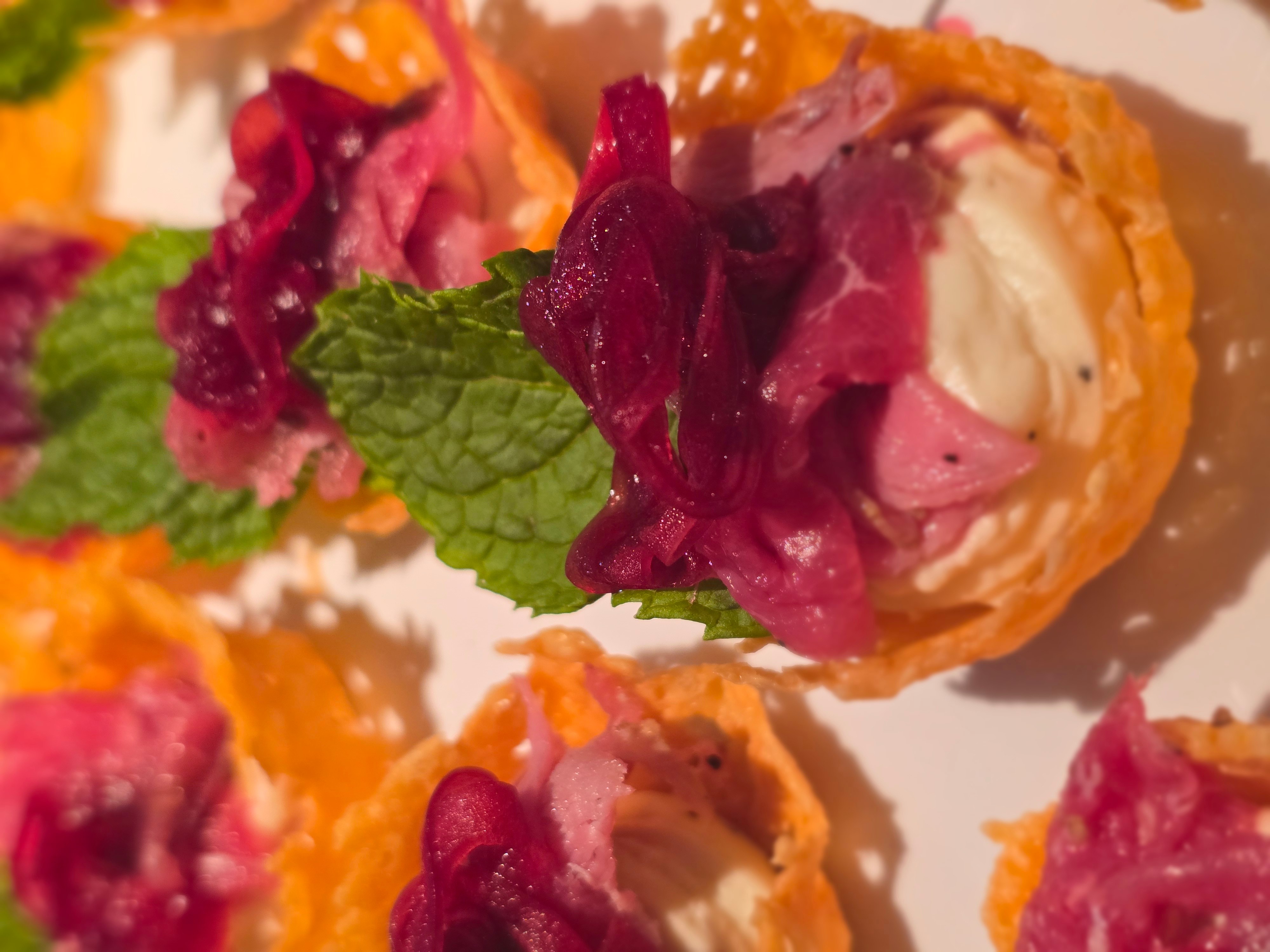 Close-up of colorful appetizer with mint leaves and pink sauce, on a white plate.