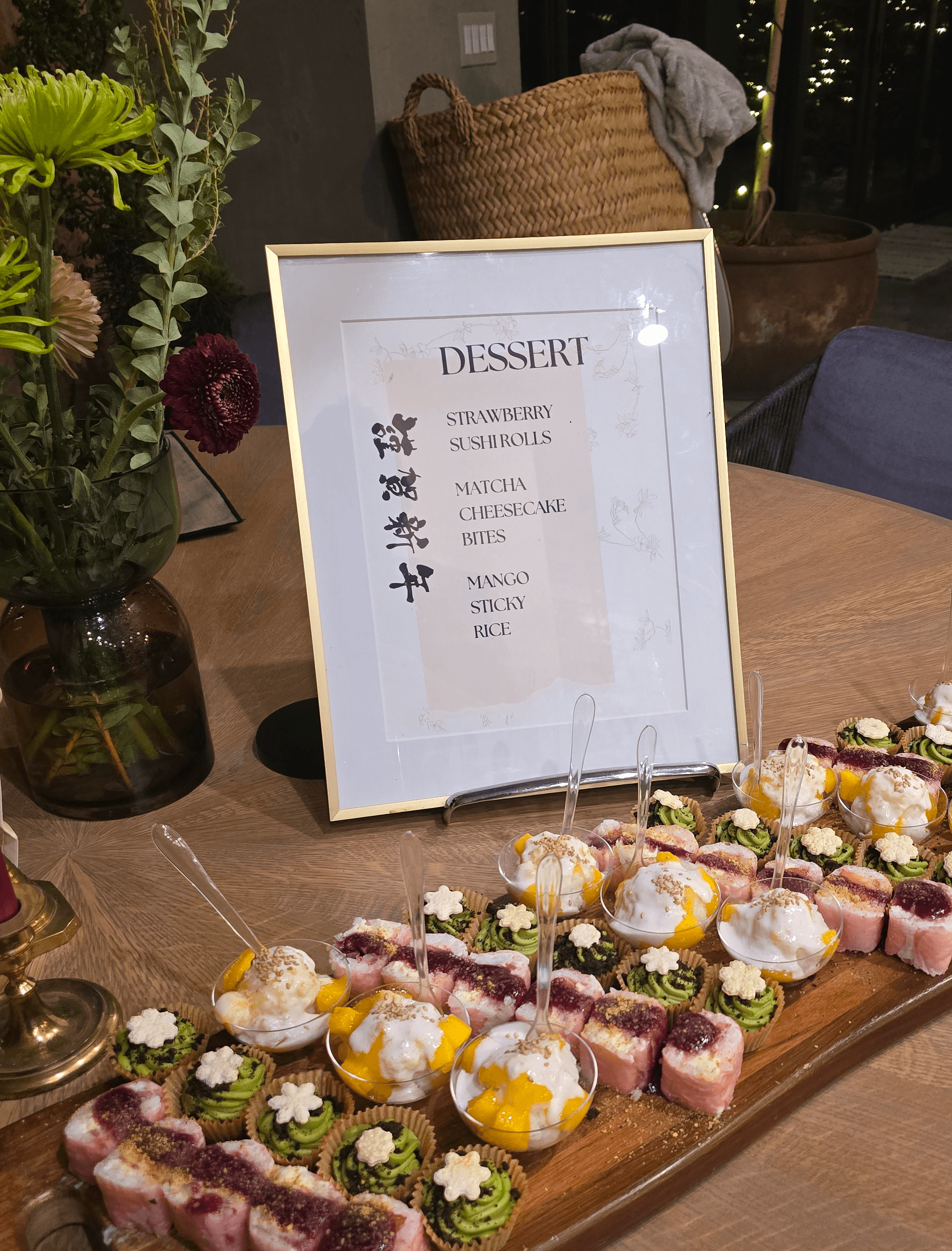 Framed dessert menu on table with assorted desserts including cakes and pastries, and a vase with flowers nearby.