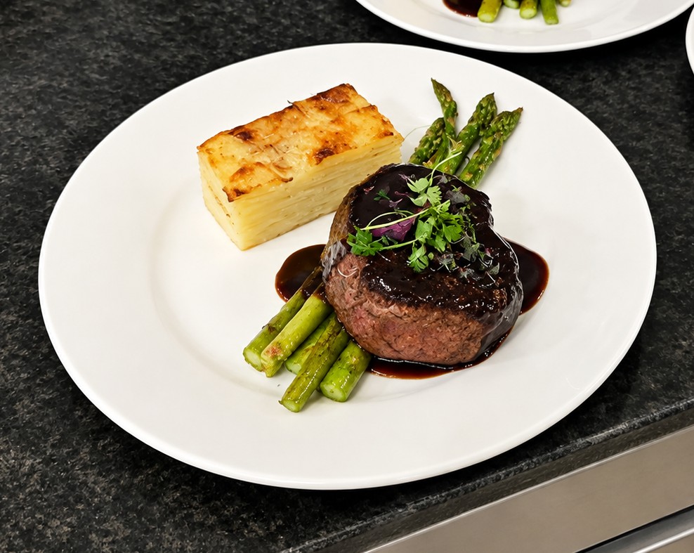 Steak with asparagus, potato gratin, and sauce on a white plate.