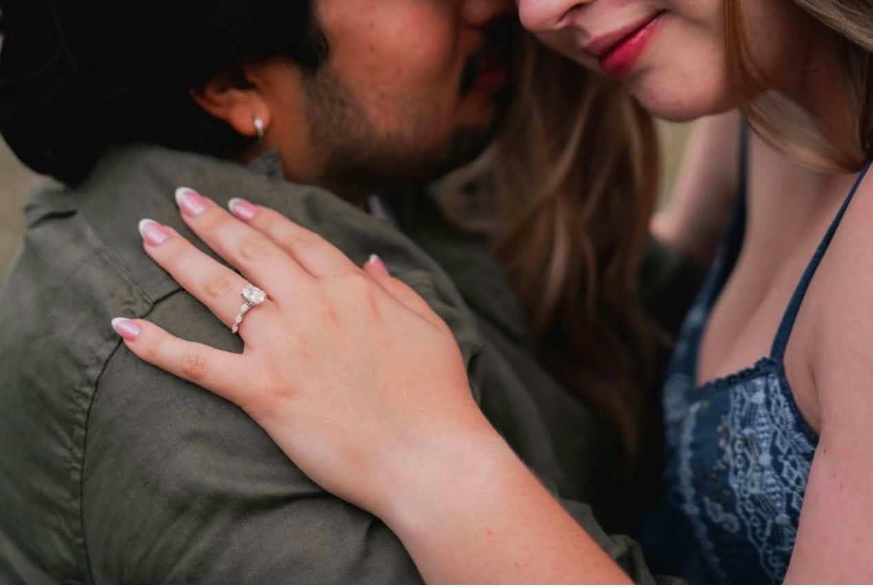 Close-up of a woman with a ring on her finger touching a man's shoulder, both leaning close together.