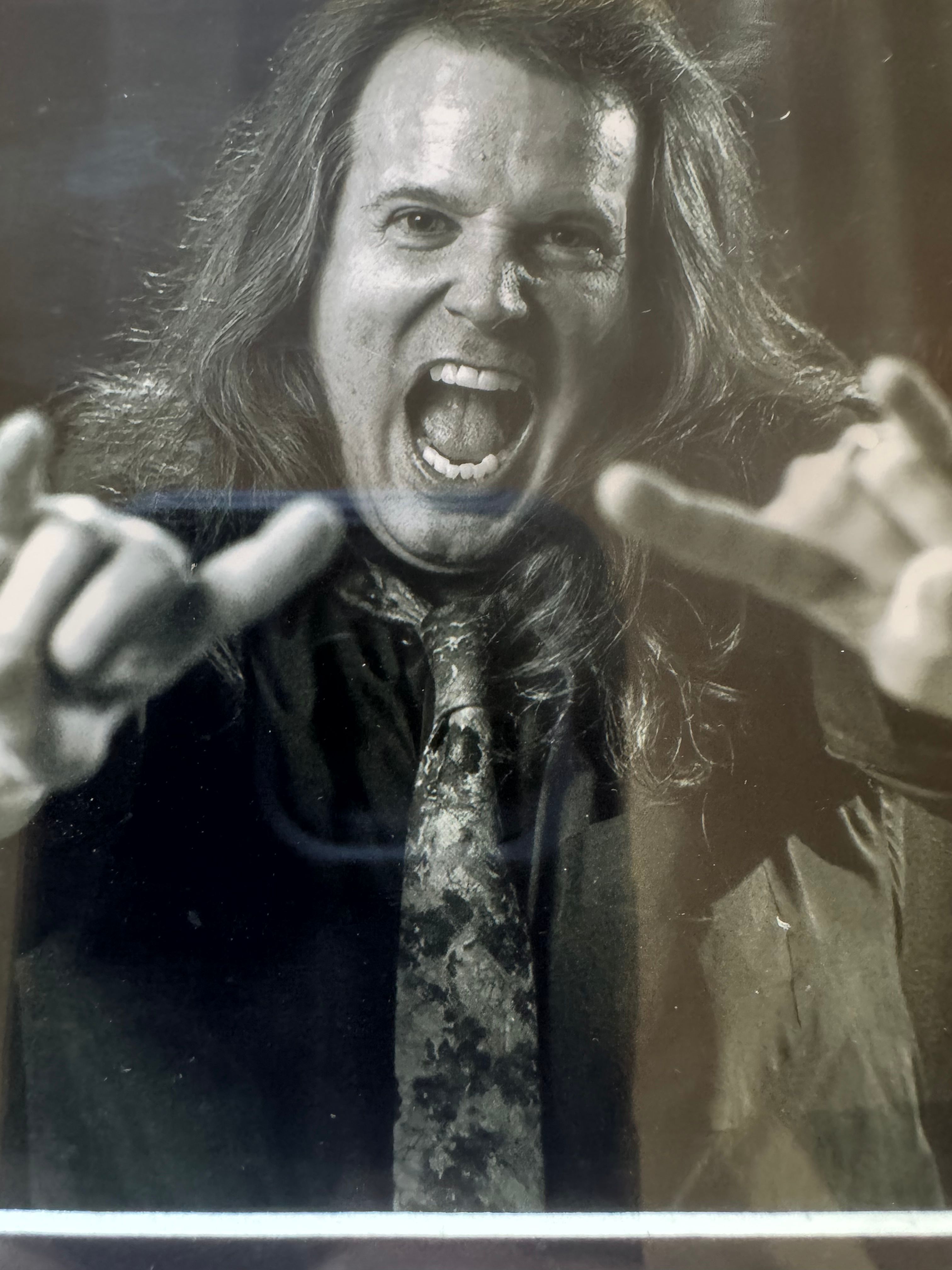 Woman with long hair shouting and pointing fingers, wearing a dark jacket and tie, in black and white.
