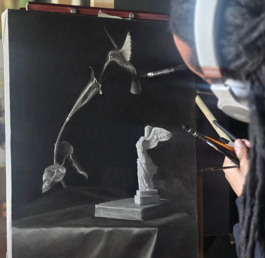 Artist painting a still life of a statue and a plant on a black background, with a brush in hand, seen from the side.