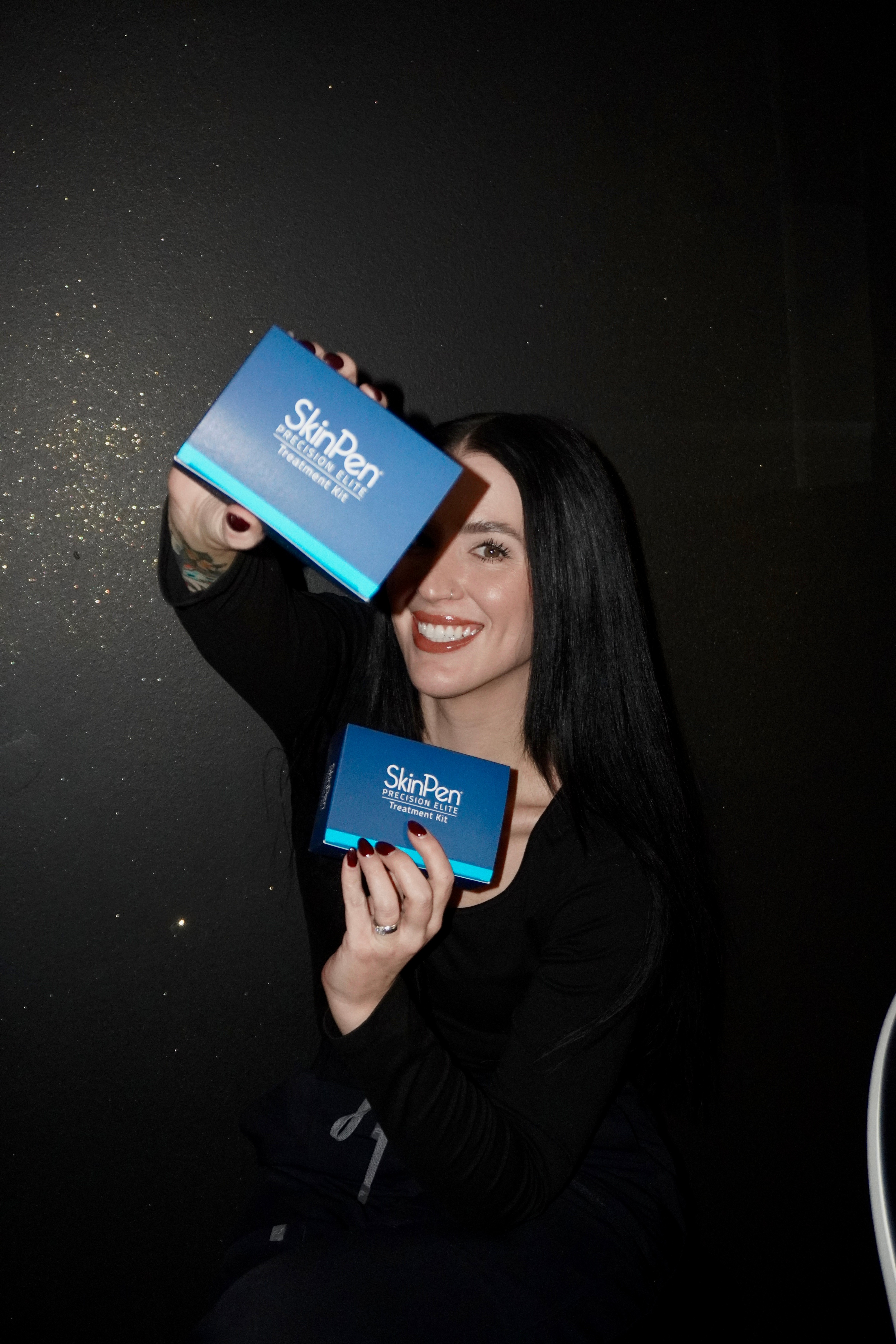 Woman with black hair smiling, holding two blue cards with white text, against a dark background.