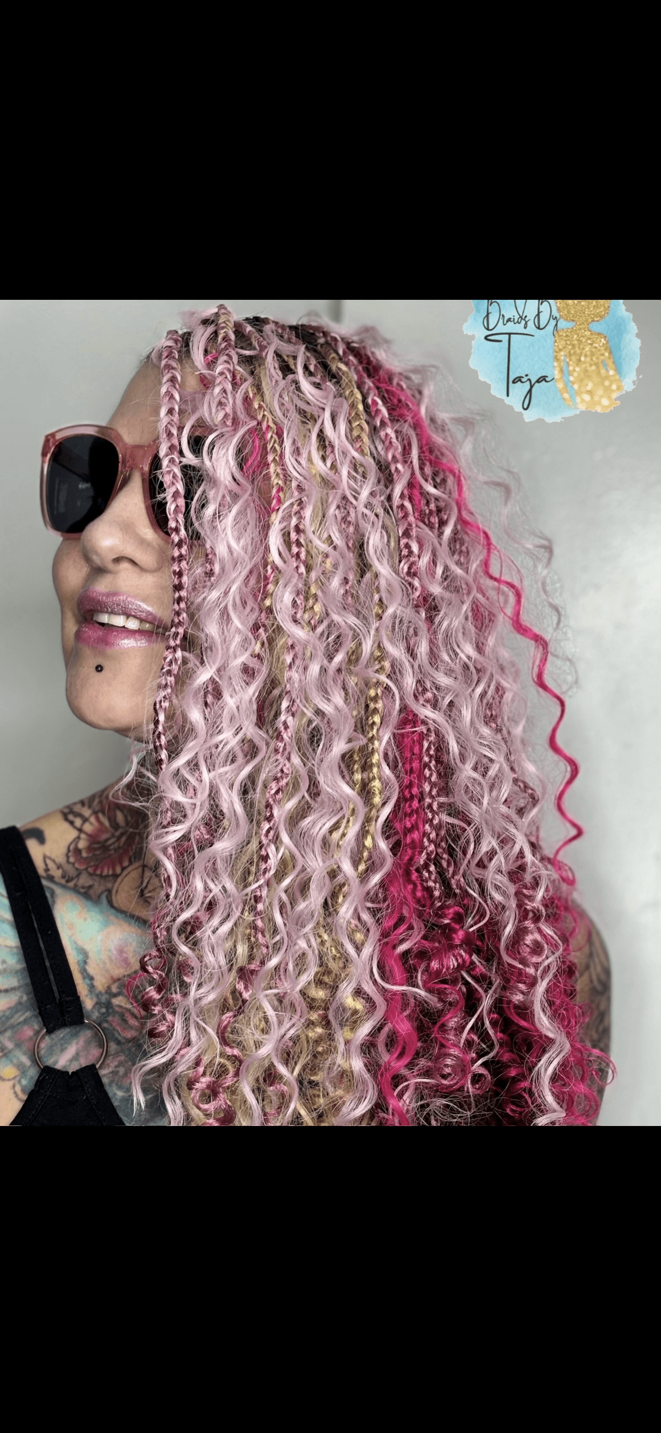 Person with curly pink and blonde hair, wearing sunglasses, smiling, and a black top.