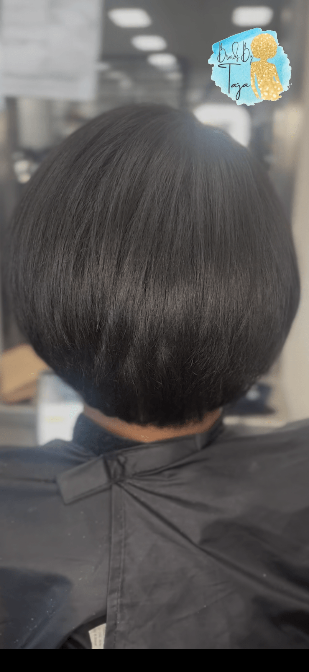 Back of a person's head with a short, dark, straight hairstyle in a salon setting.