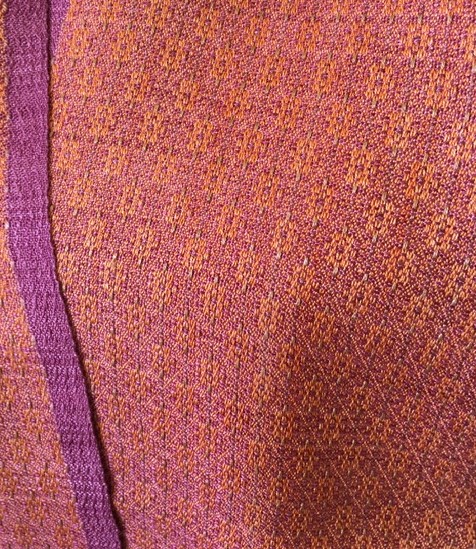Close-up of a textured, multicolored fabric with purple and orange hues, showing detailed weave pattern.