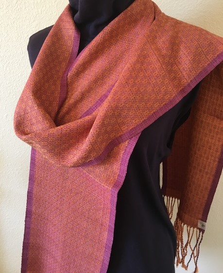 A mannequin displays a two-tone shawl with a reddish-brown and purple border draped over a black outfit.