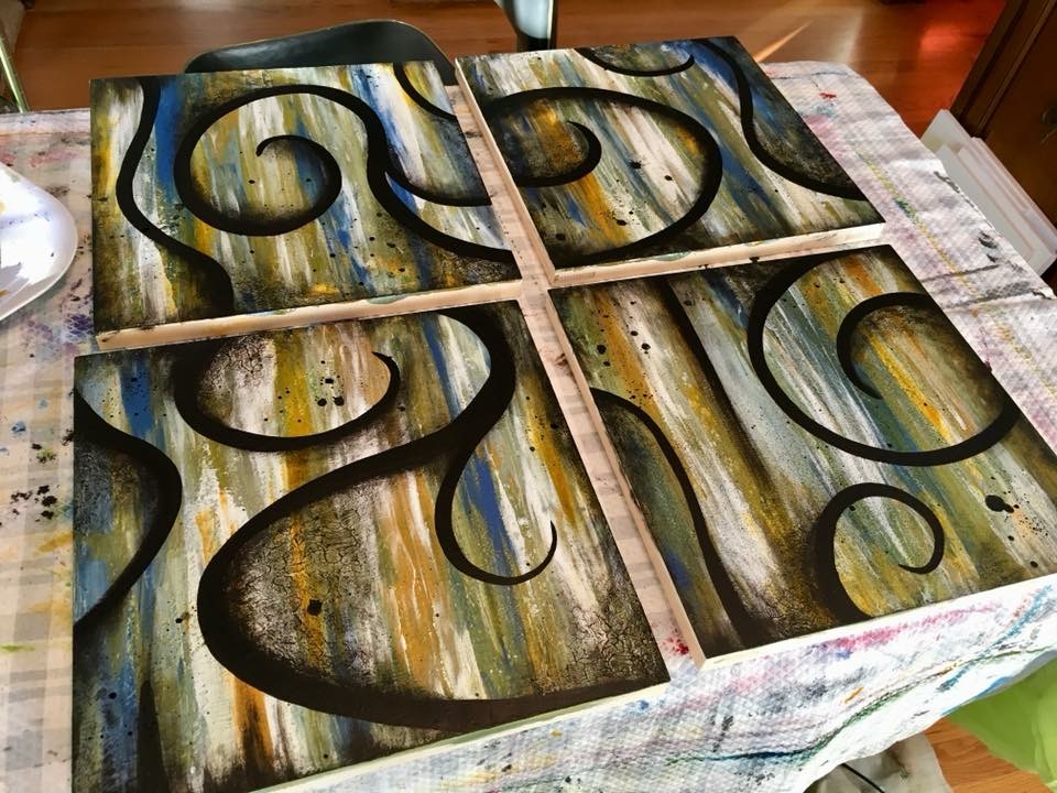 Four abstract paintings with swirling black lines and colorful backgrounds on a table, with a cloth underneath.
