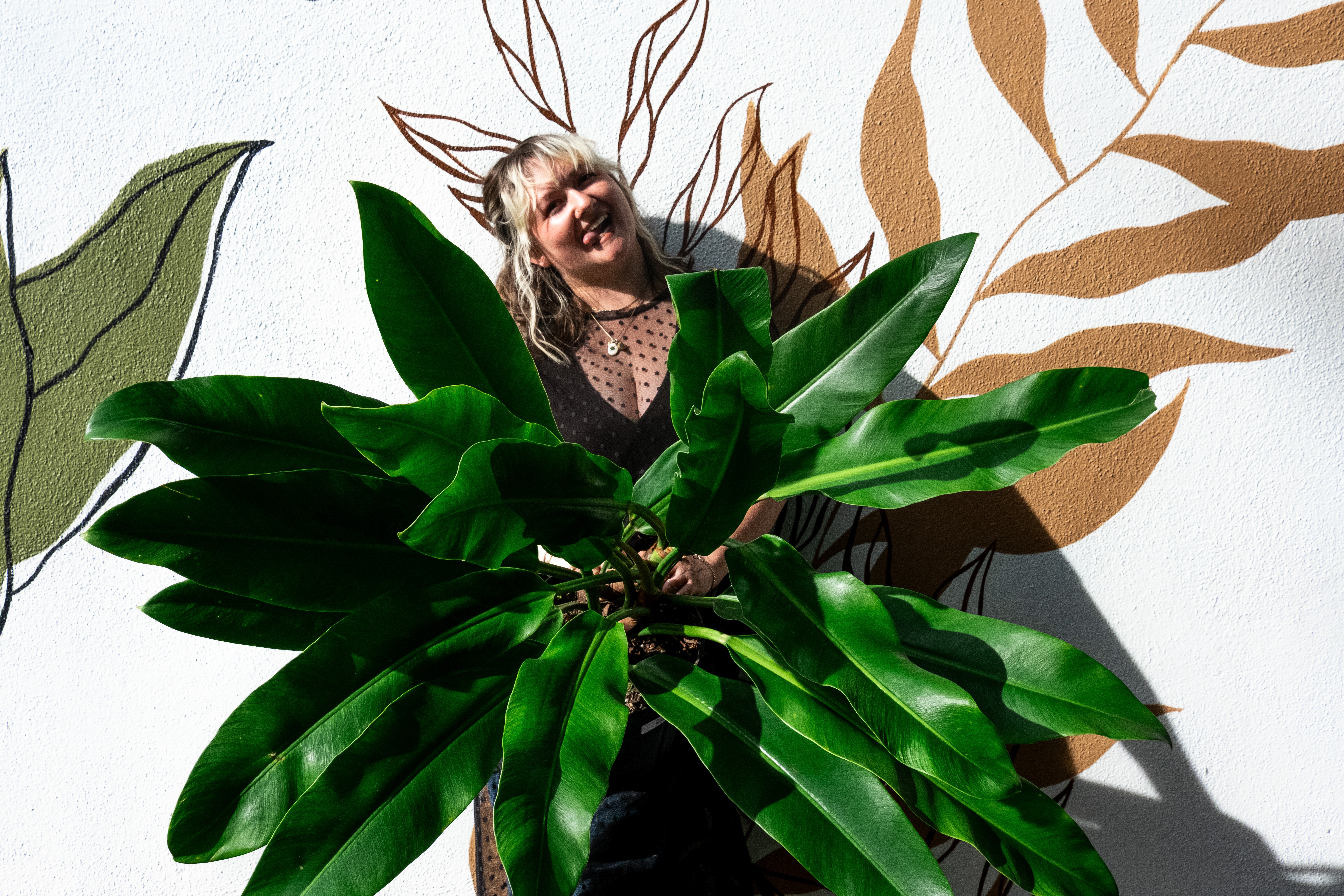 Person with short hair and glasses behind large green leaves, with a background of abstract leaf illustrations.