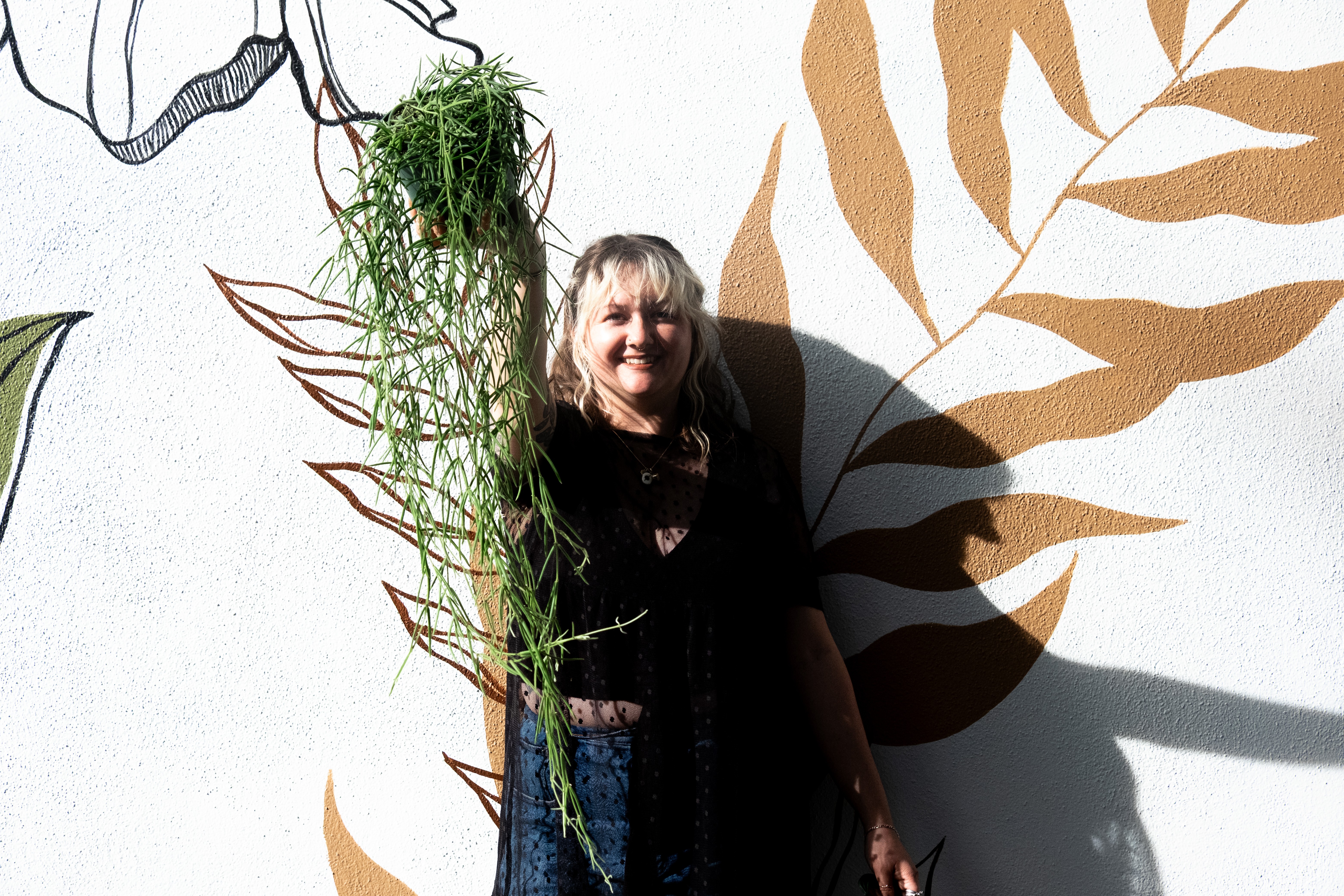 Woman standing in front of a wall with large painted leaf designs, smiling, with shadows cast on the wall.