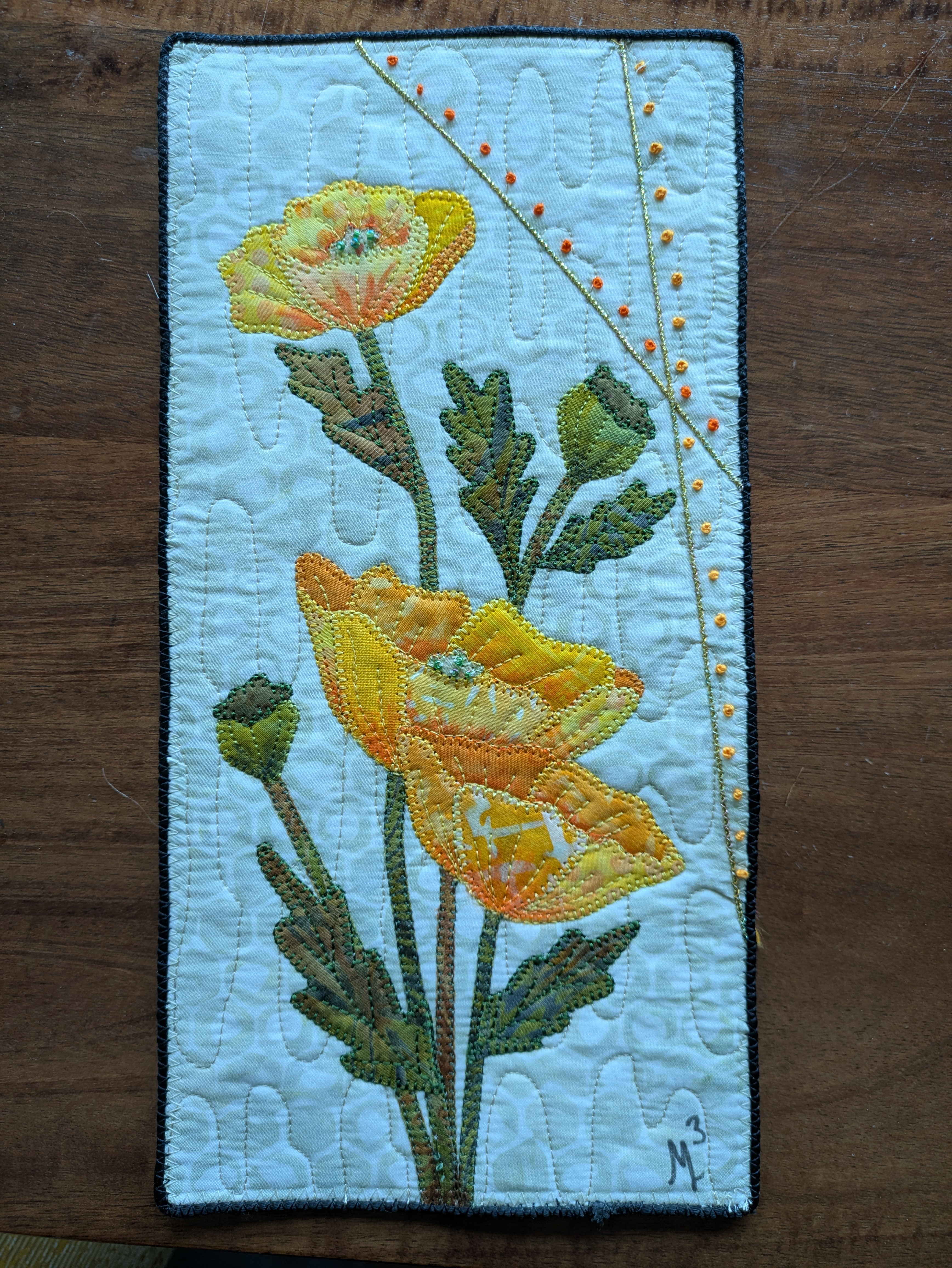 Vertical quilted fabric panel with embroidered yellow flowers and green leaves on a light blue background.