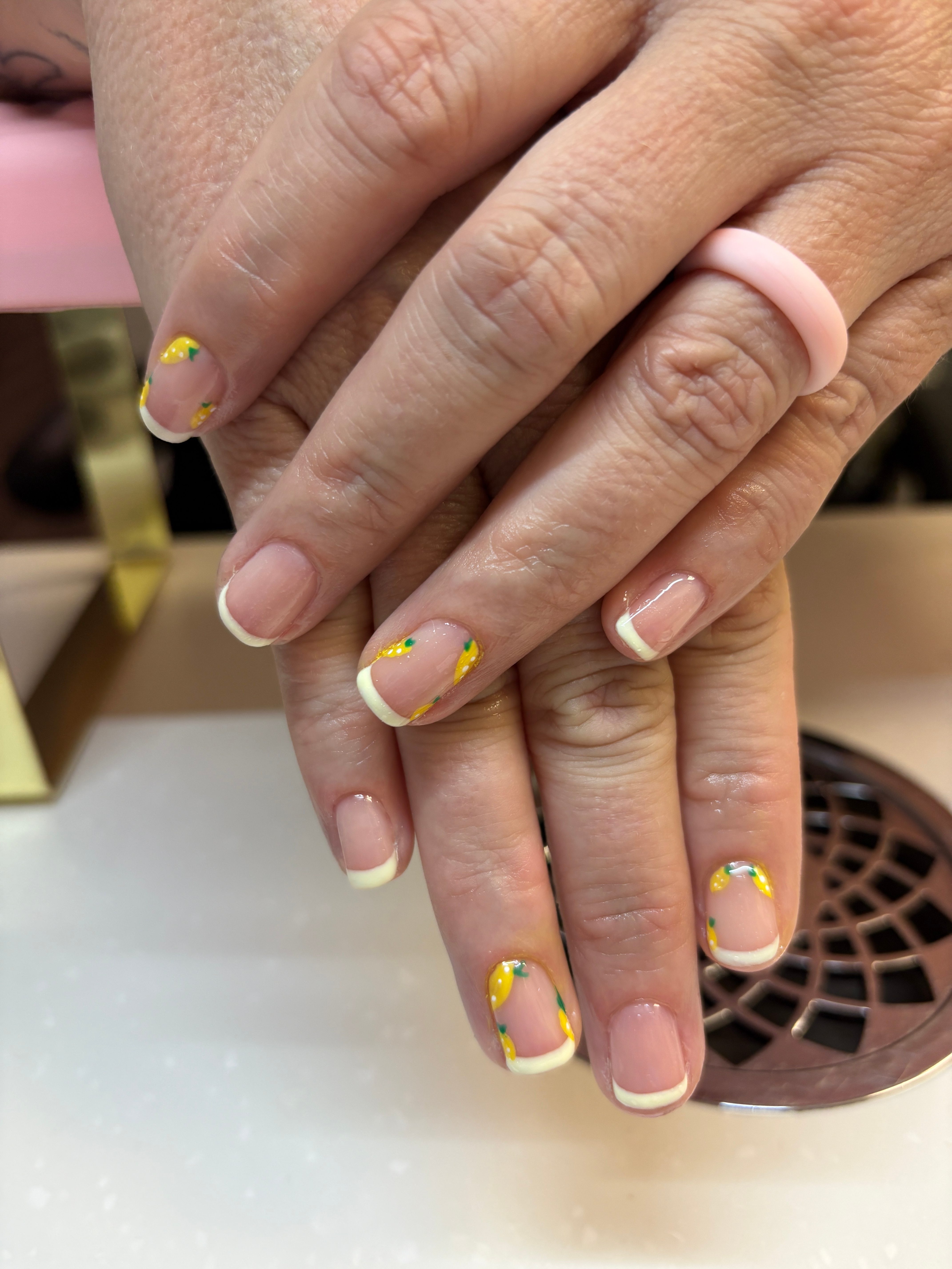 Hands with decorated nails resting on a white surface, with a vent in the background, showing a colorful nail design.