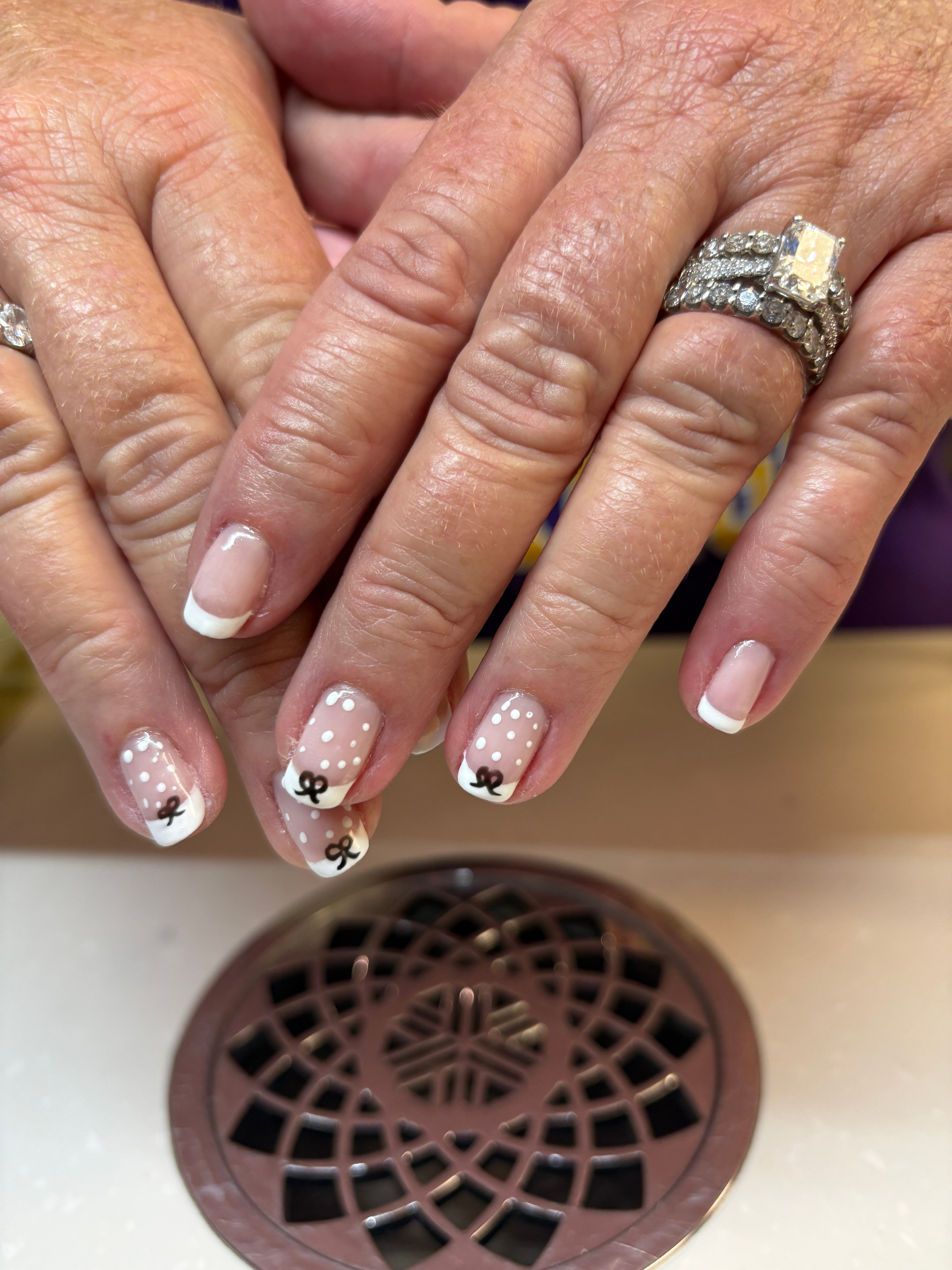 Close-up of hands with decorated nails and rings, near a circular vent on a beige surface.