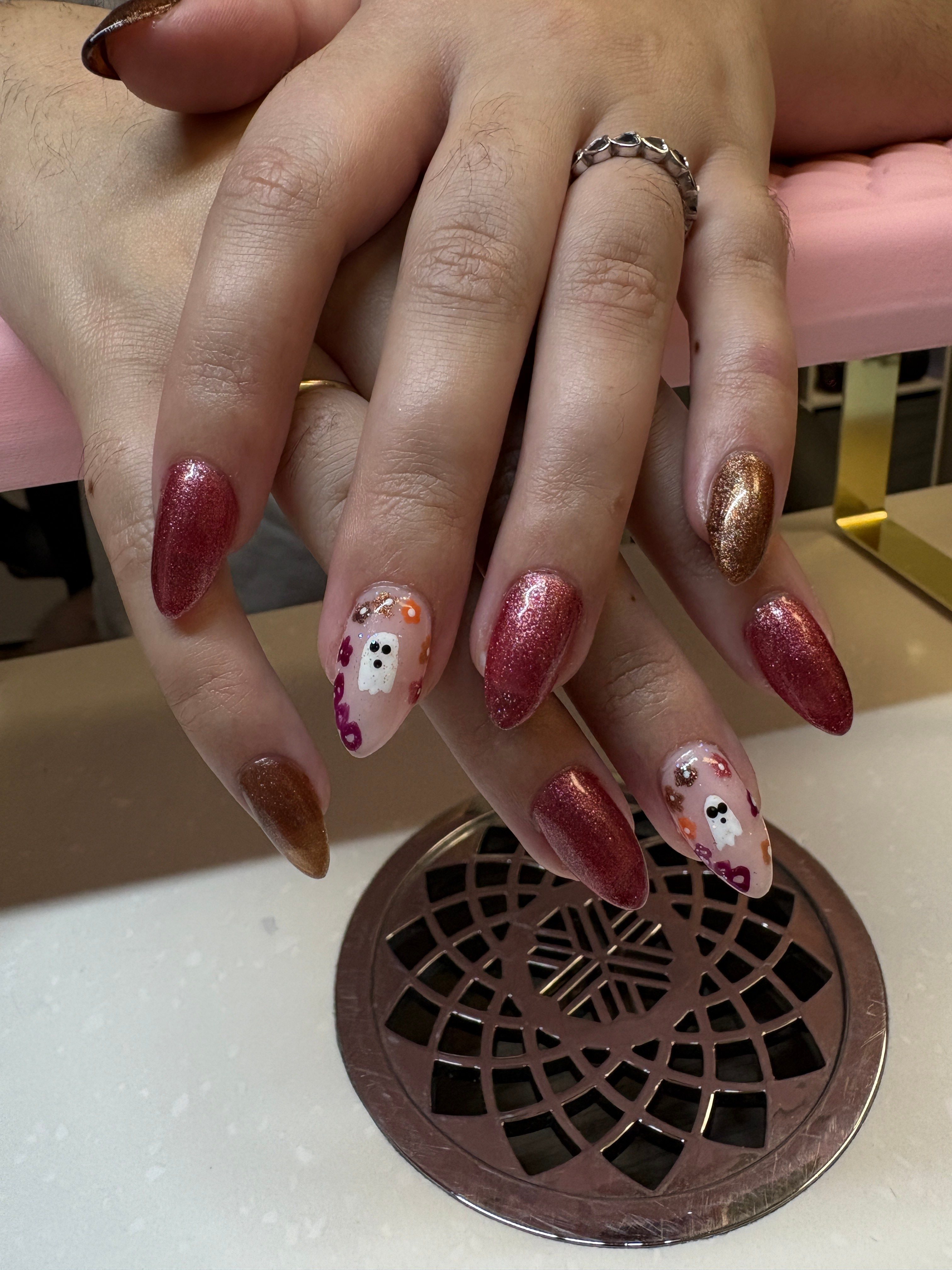 Hand with decorated nails near a circular drain on a white surface.