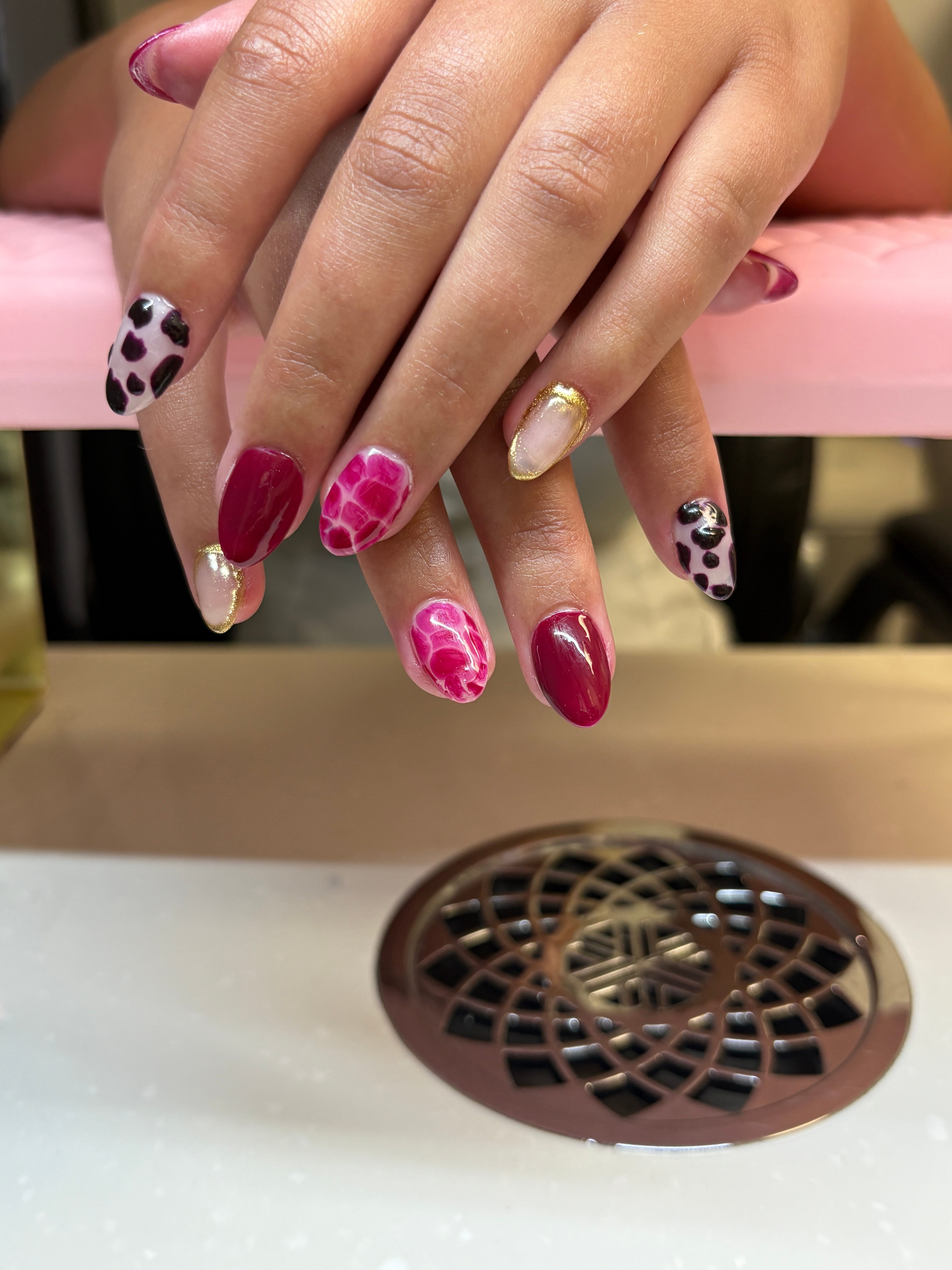 Close-up of hands with decorated nails near a white surface with a brown vent, showing various nail designs and colors.