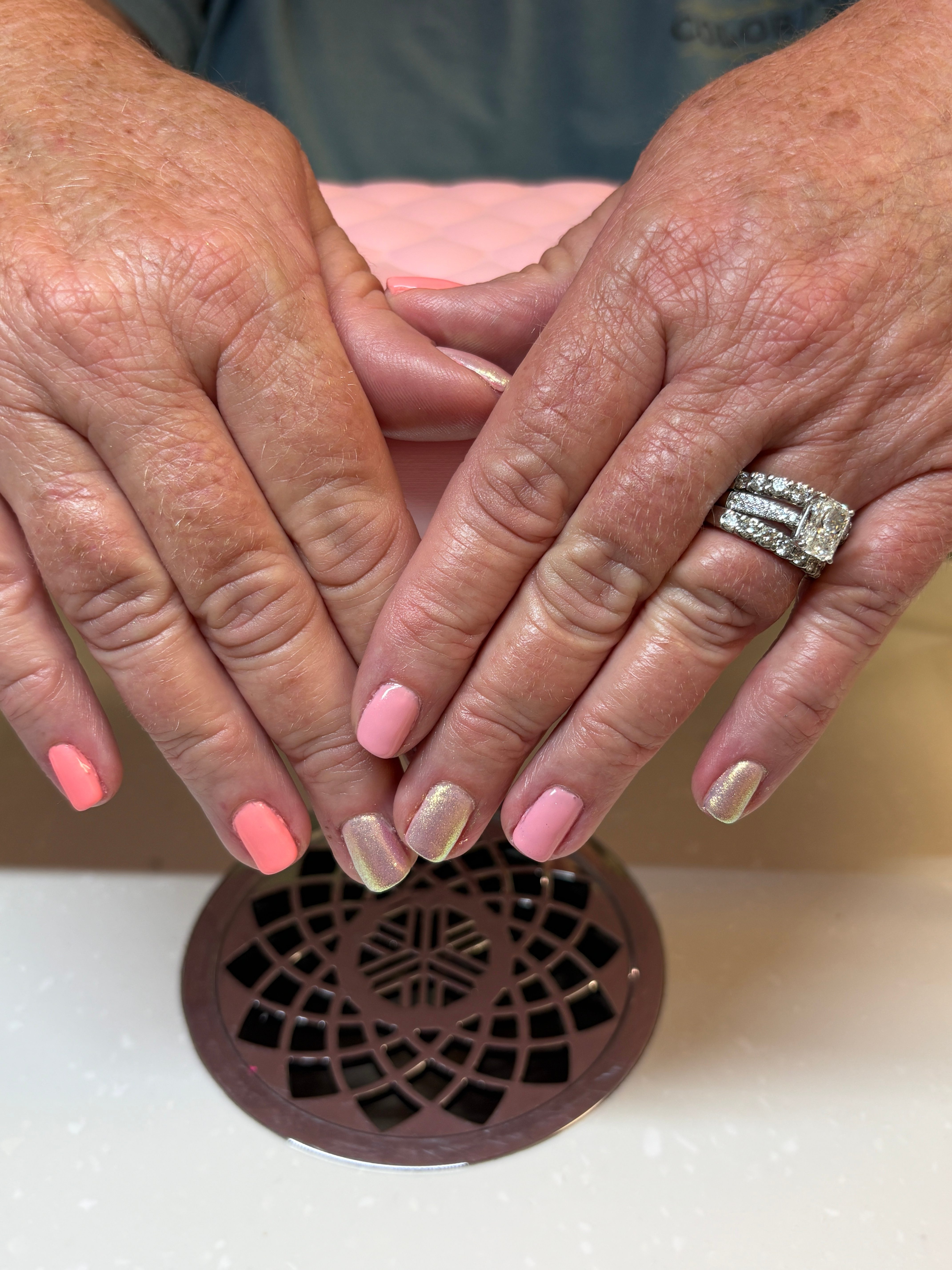 Two hands with manicured nails touch near a circular drain cover on a beige surface.