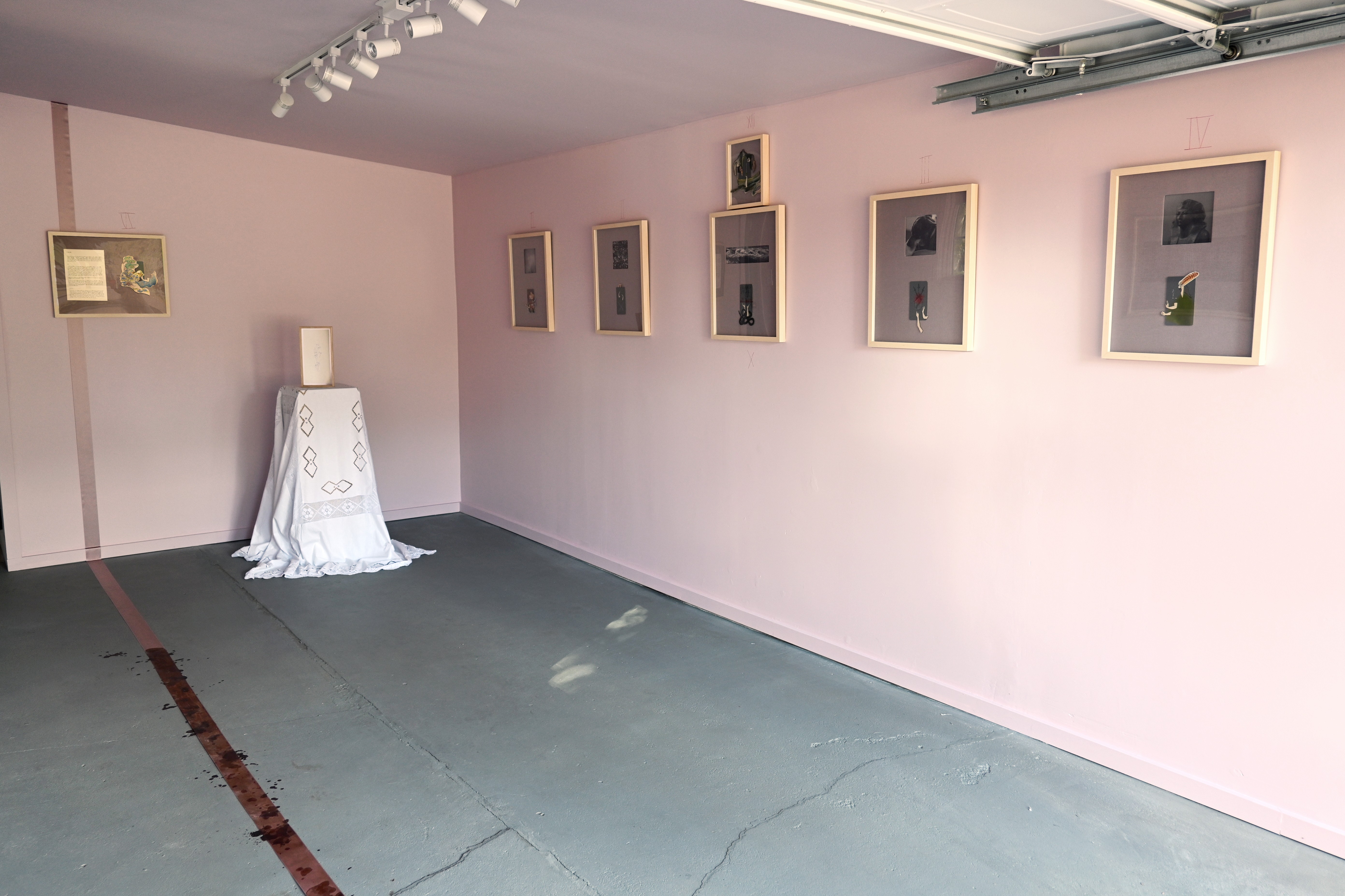 Gallery with framed artwork on pink walls and a white pedestal with a cloth, floor has visible cracks.