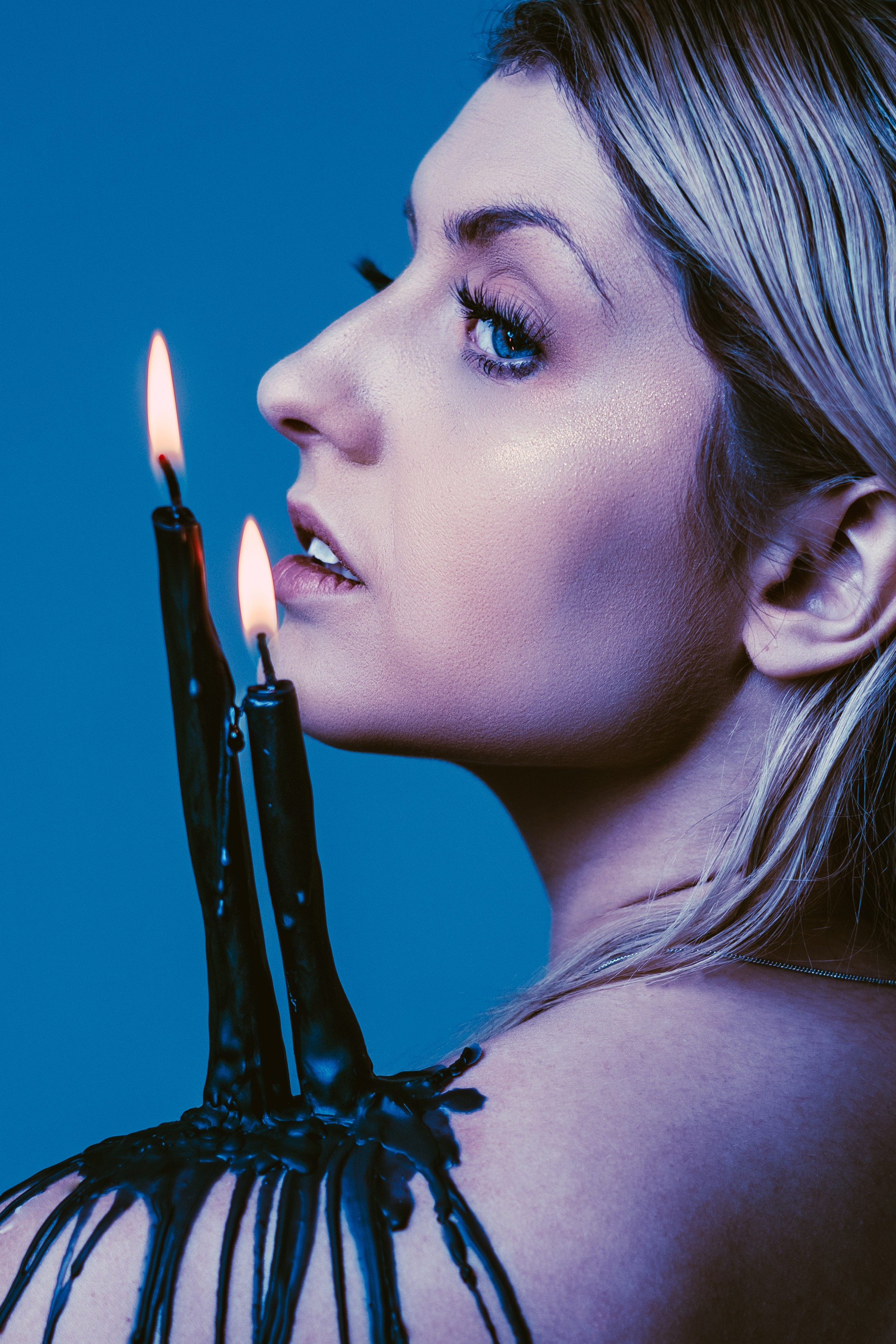 Woman with candles on her fingers, looking sideways, with a blue background.