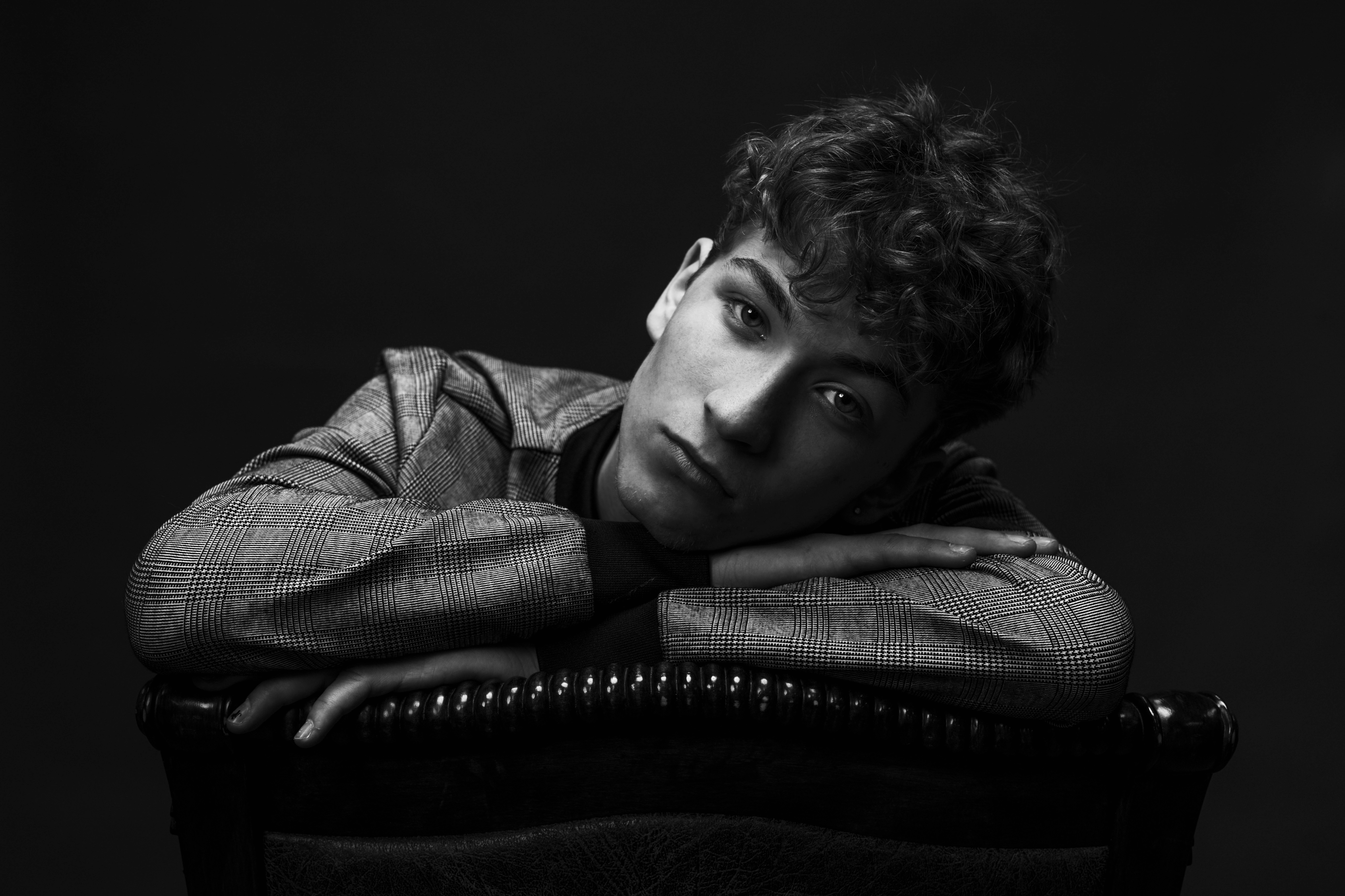 Young man with curly hair resting his head on his arms, looking at the camera, in black and white.