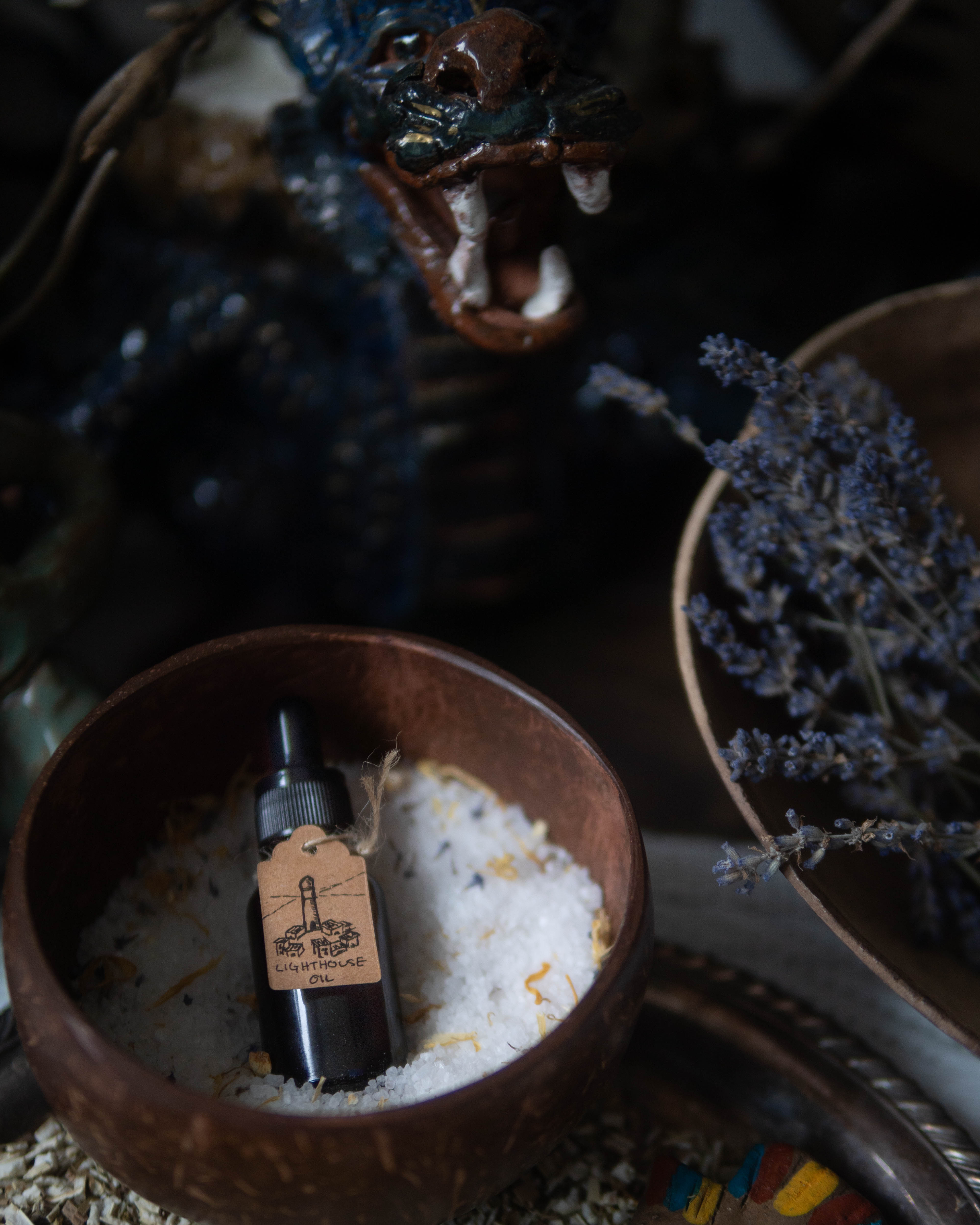 A small bottle with a dropper inside a wooden bowl filled with white substance, next to a potted plant with purple flowers.