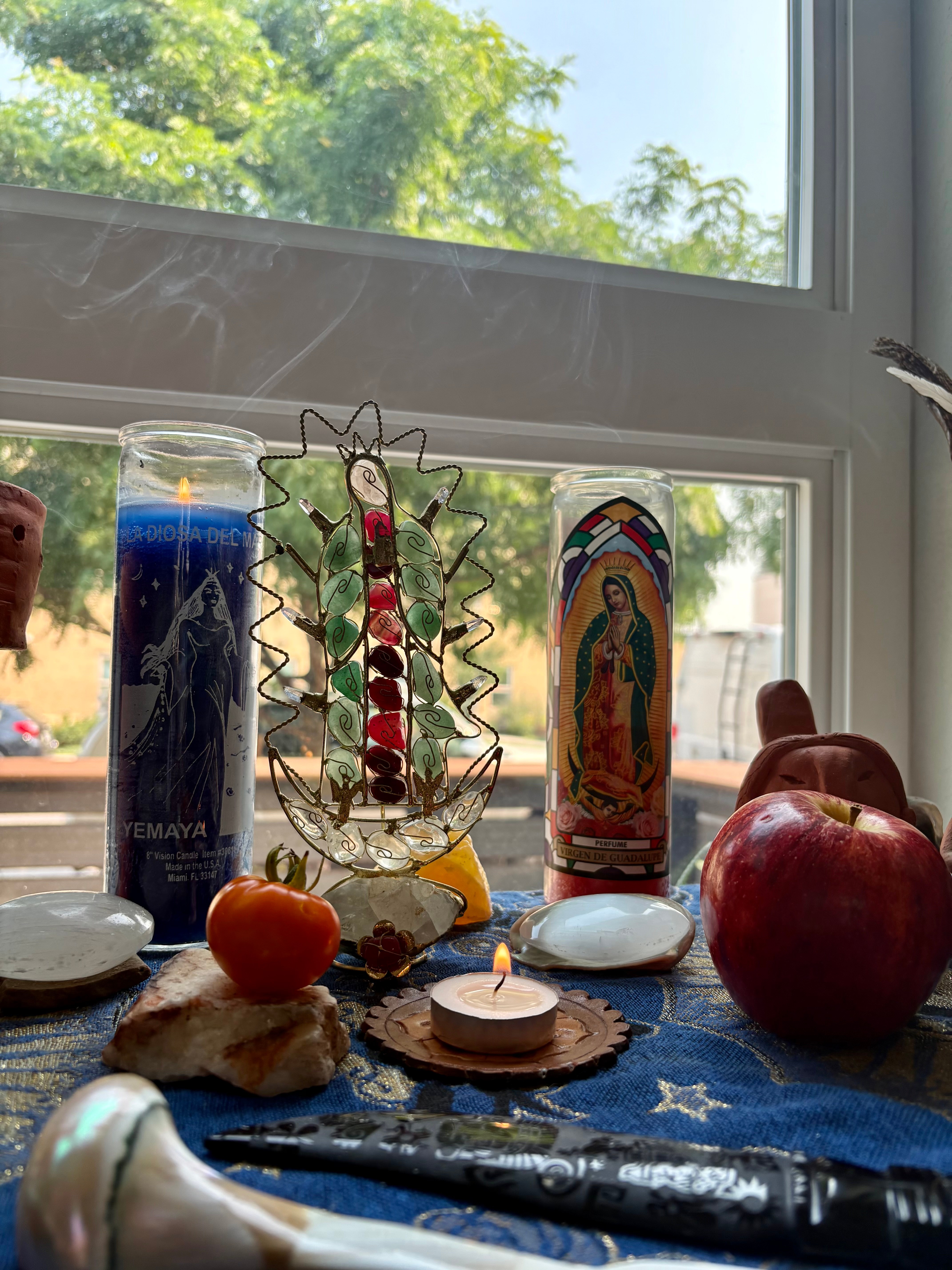 Candles, apples, and decorative items on a windowsill with trees outside, sunlight shining through the window.