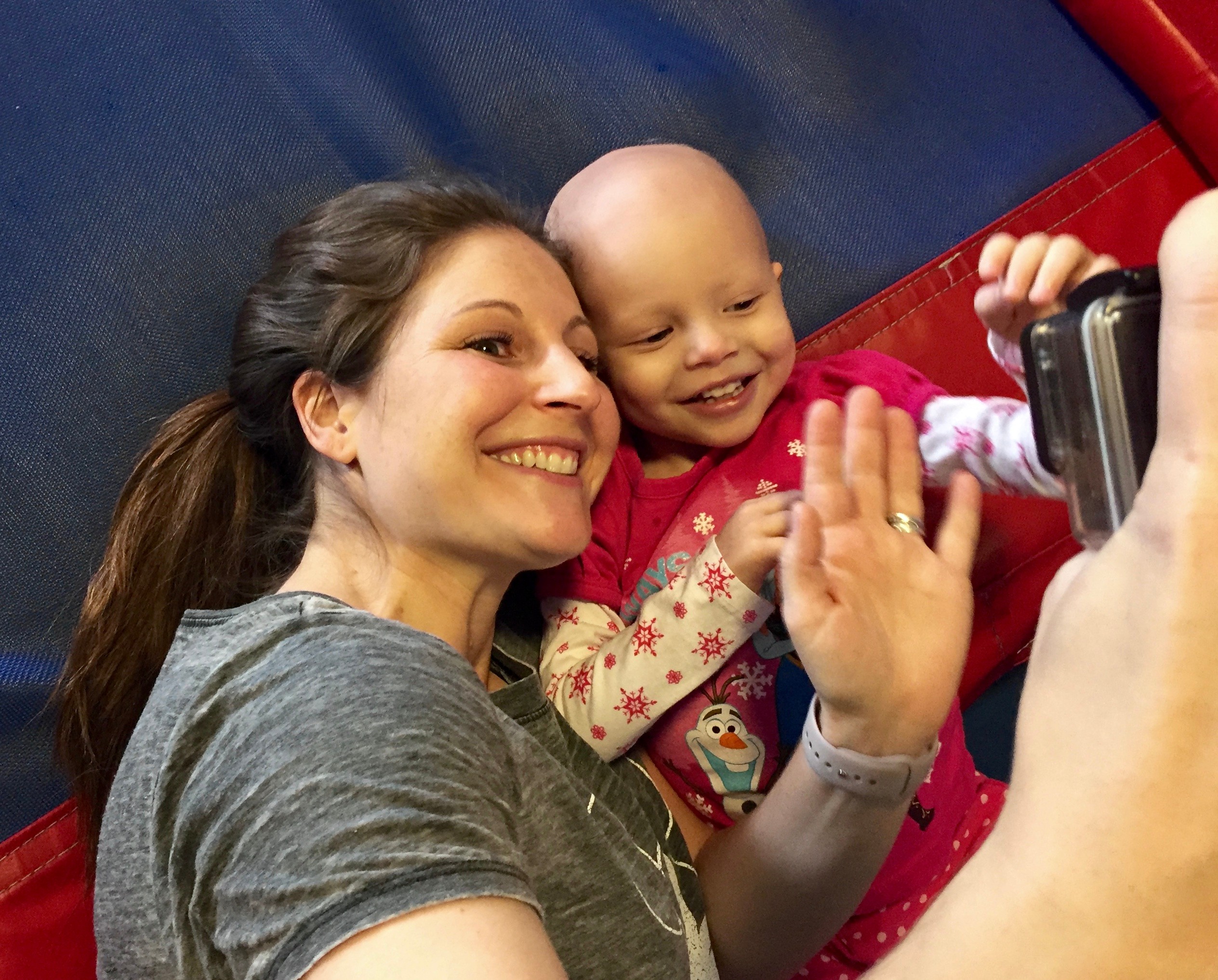 Woman and child smiling and waving at a camera, lying on a colorful surface.