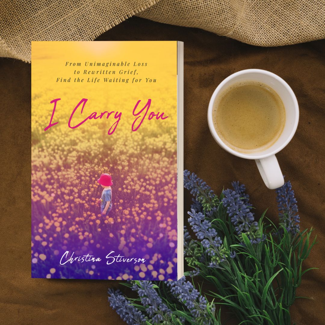 Book titled 'I Carry You' with a person in a field of flowers, next to a cup of tea and lavender flowers.