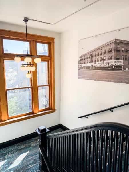 Corner of a room with a large window, black railing staircase, and a black-and-white cityscape photograph on the wall.
