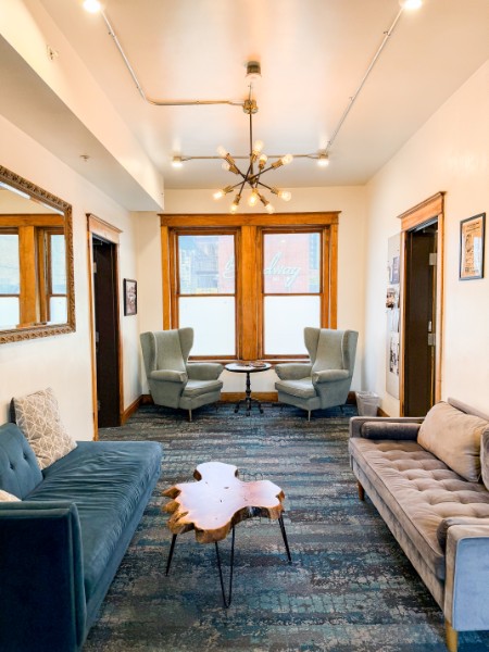 Living room with two armchairs facing large windows, a blue sofa, a gray sofa, and a wooden coffee table, with a ceiling fan.