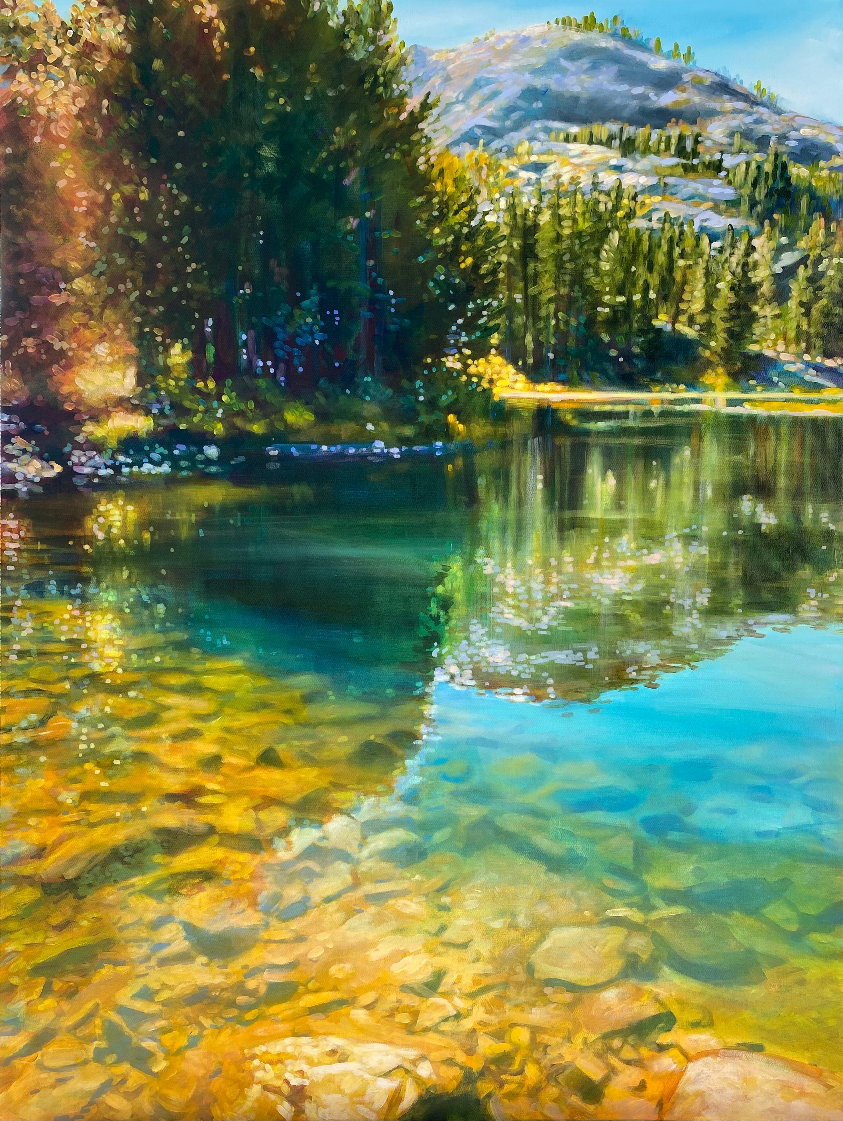 Scenic landscape with a clear lake, trees, mountains, and a blue sky, reflecting the surroundings.