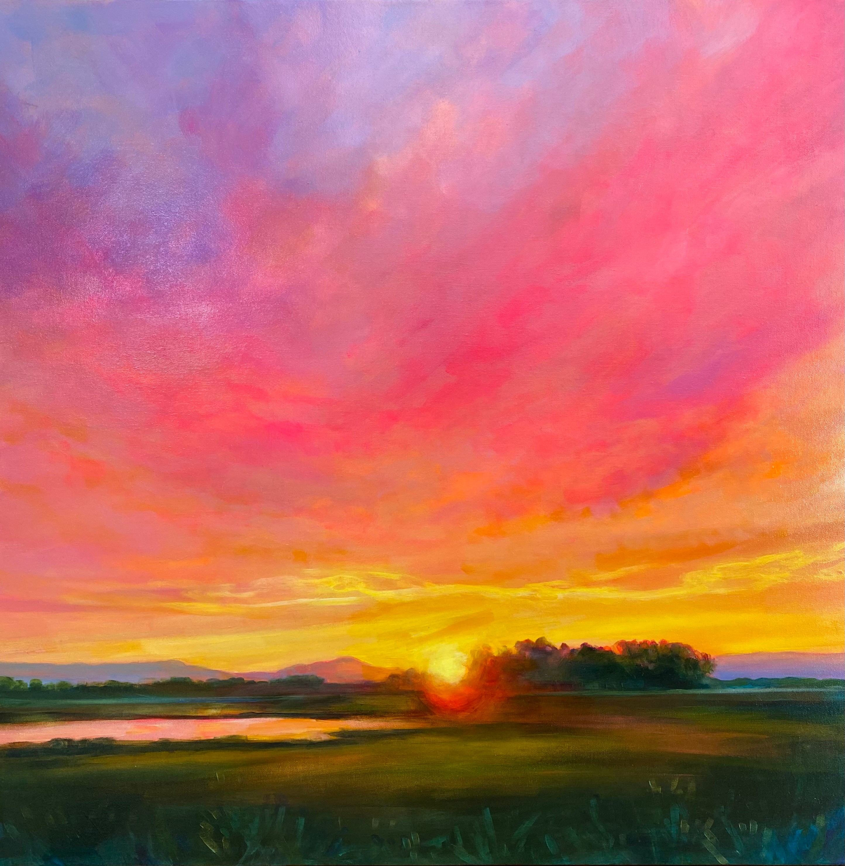 Sunset over a landscape with colorful sky, clouds, and a body of water, with trees and grassy fields in the foreground.