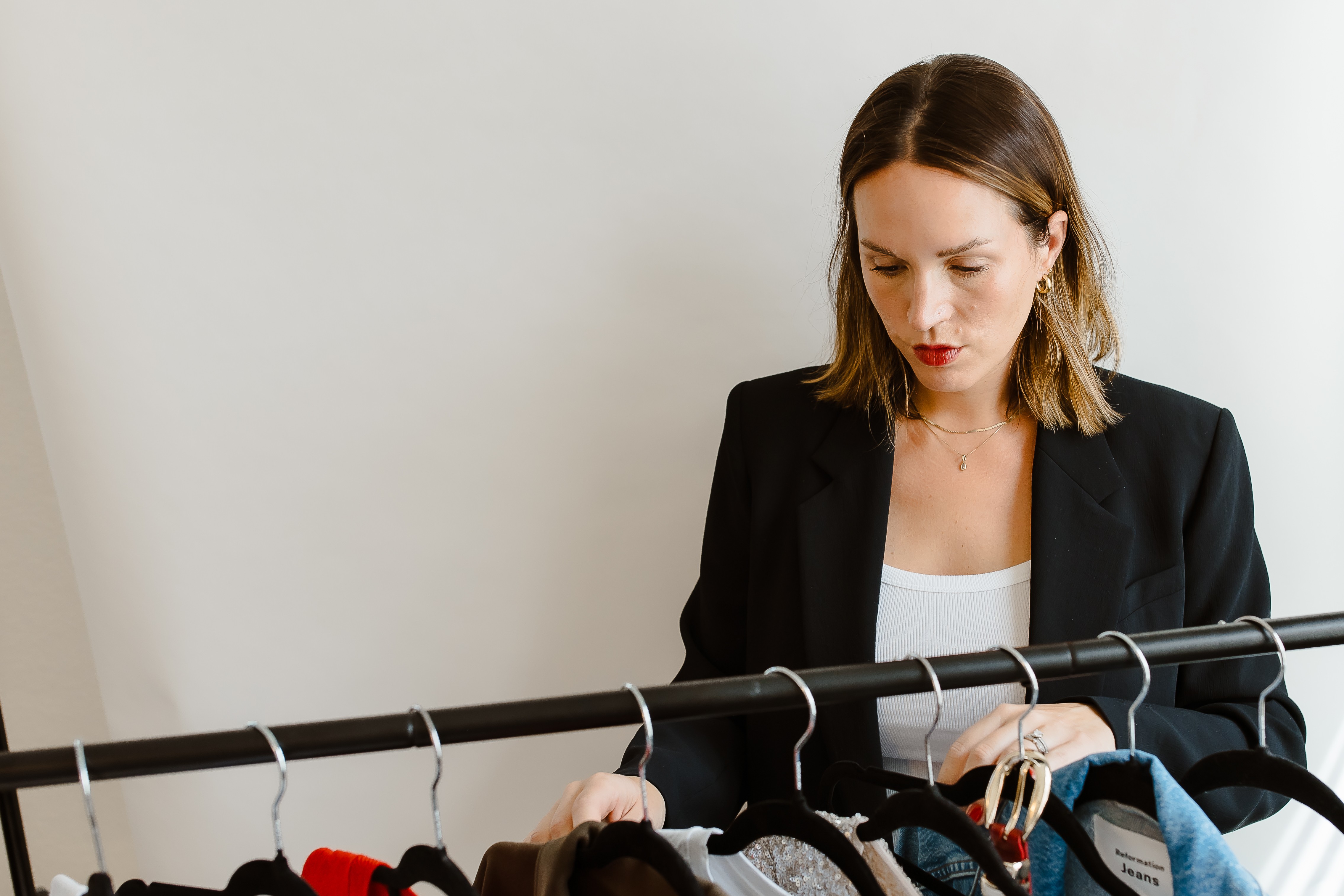 Woman with shoulder-length hair in a black blazer looking at clothing on a rack.