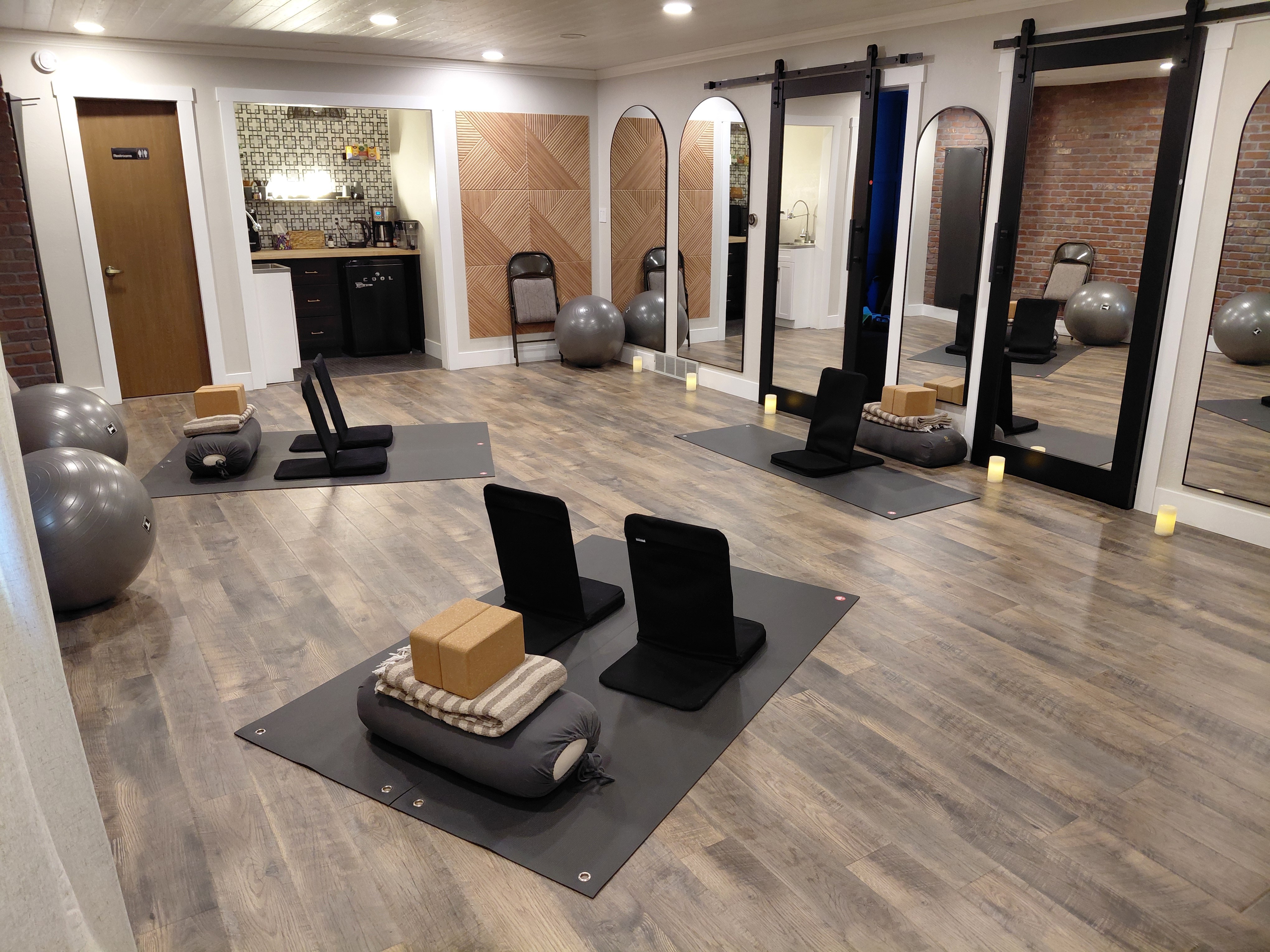 Fitness studio with mats, blocks, and exercise equipment, mirrors, and a wooden floor.