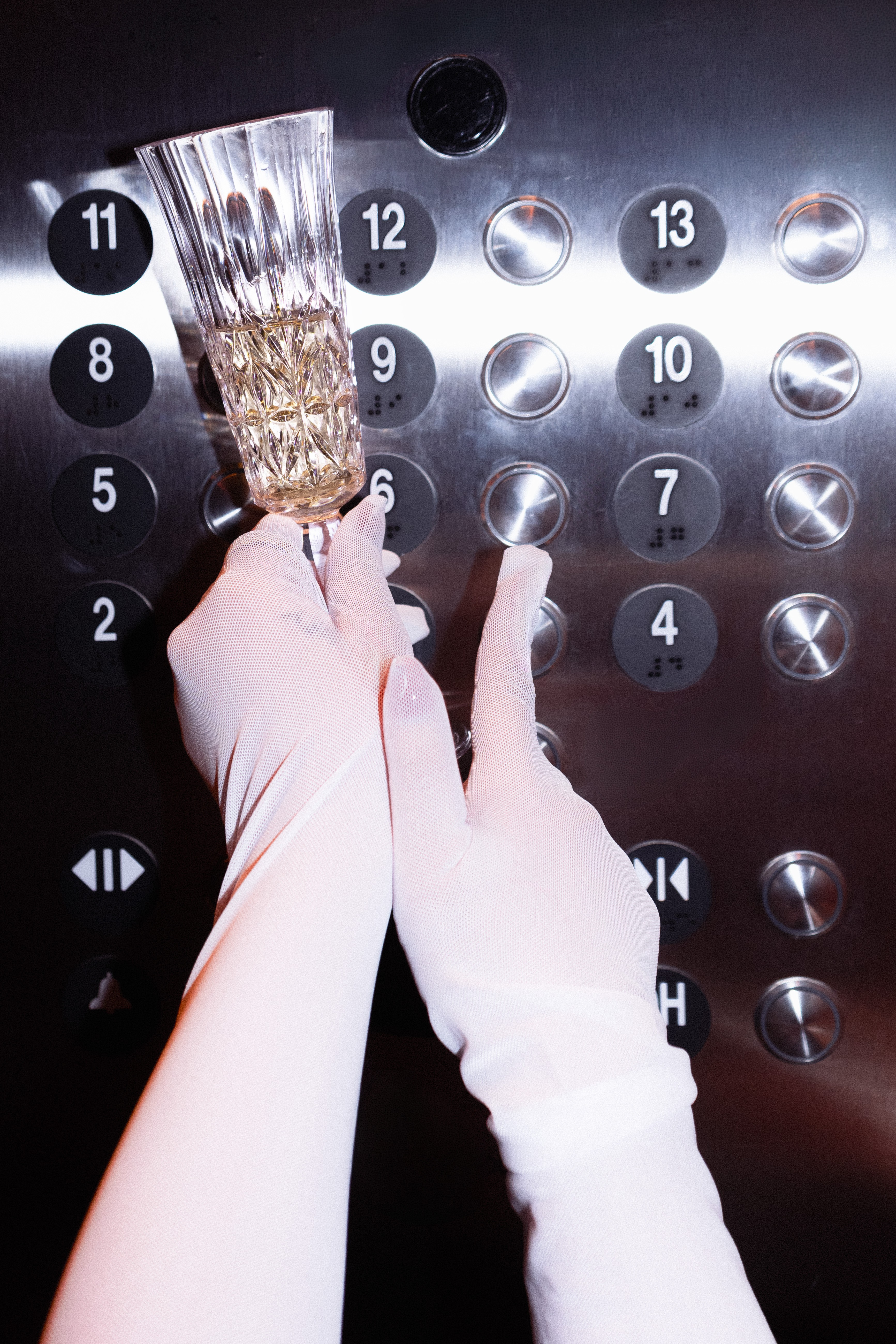 Person pressing elevator button with a brush in hand, elevator panel with numbered buttons, one hand wearing a white glove.